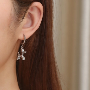 Close-up of a silver balloon dog charm earring worn by a model in a trendy style