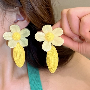 Detail of yellow woven raffia flower earrings with tassel leaves on model ear
