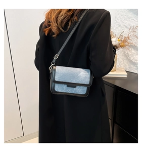 Detail of blue denim shoulder bag with black leather trim and metal hook buckle