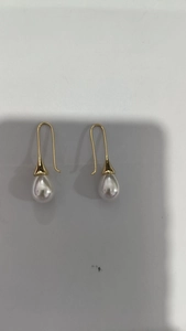 Detail view of gold drop earrings with white teardrop pearls and elegant long hook design