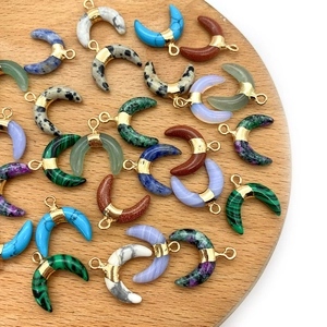 Natural crescent moon stone pendants in assorted colors with gold bails on wood