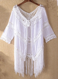Detailed close-up of white crochet beach cover-up with bohemian tassel hem on wooden hanger
