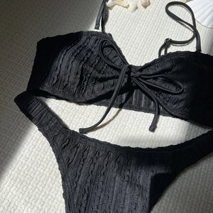 Detailansicht des schwarzen Bikini-Sets mit Wellenstruktur und Schleife auf weißem Stoff
