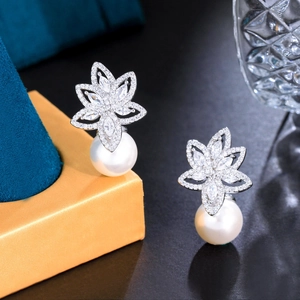 Detail of flower-shaped earrings with micro-pave zircons and white pearls on blue velvet