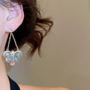Close-up of elegant gold drop earrings with pink and blue crystals worn by a model