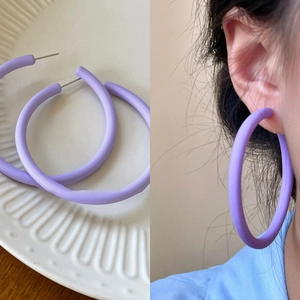 Detail view of large matte purple hoop earrings shown on tray and worn by a model