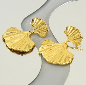 Macro detail of golden ginkgo leaf earrings with realistic vein texture on mirror base