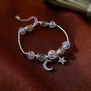 Detailed shot of cat eye bead bracelet with silver moon and star charms on fabric