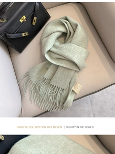 Close-up of mint green wool scarf with fringe detail and care label on beige leather