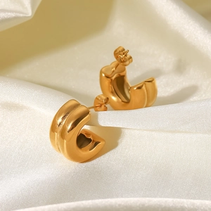 Detail eines klobigen goldenen C-förmigen Ohrrings mit Rille auf weißem Seidenhintergrund