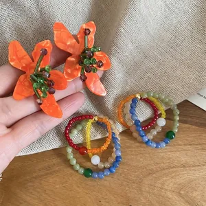 Ethnic style flower earrings with colorful beaded rings on a rustic beige background