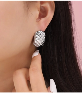 Macro shot of silver geometric diamond quilted earrings worn on the earlobe
