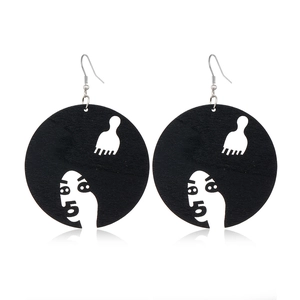 Detailed view of black wooden earrings with white carved face silhouette and comb design