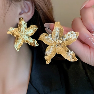 Macro shot of oversized gold flower earrings featuring detailed metallic petal texture