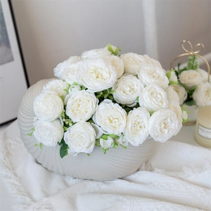 White silk peonies in shell-shaped ceramic vase on soft fabric background