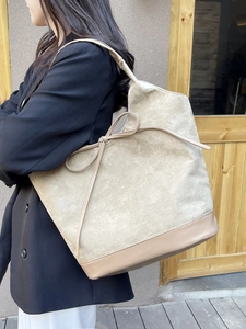 Beige suede tote bag with side bow detail worn by a model in casual outdoor setting