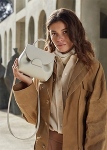 Polished beige leather handbag featuring a unique round buckle and flap closure