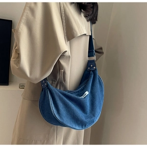 Detail of dark blue denim half-moon bag on khaki coat with silver metal hardware detail