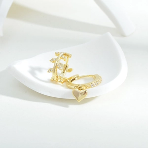 Close-up of gold earrings with heart pendant and leaf design featuring cubic zirconia details