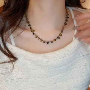 Détail du collier en pierre d'oeil de tigre irrégulière sur un pull blanc