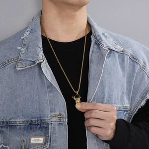 Detail of a golden astronaut pendant on a ball chain paired with a blue denim jacket