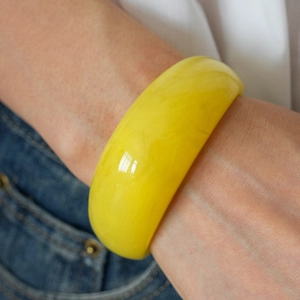 Detail view of a chunky translucent yellow resin bangle on a wrist for a modern look