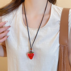Detail of red resin strawberry pendant necklace with green leaf on a black thin cord