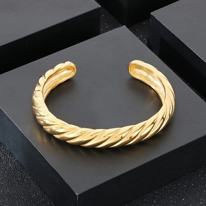Détail macro du bracelet torsadé doré en acier titane 18k sur un support noir mat