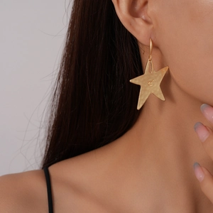Close-up of matte gold star-shaped drop earring worn by a model with hook design