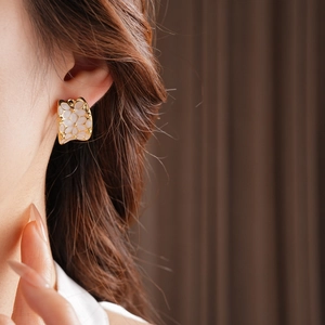 Gros plan de boucles d'oreilles fleurs dorées avec émail blanc sur le lobe d'oreille