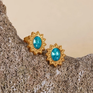 Detailed view of gold sunburst earrings featuring blue oval gemstones on rock texture