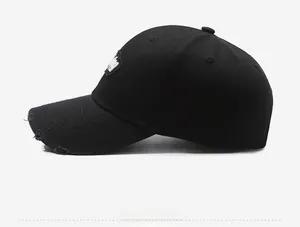 Side view of black distressed baseball cap with ripped brim and white embroidered patch