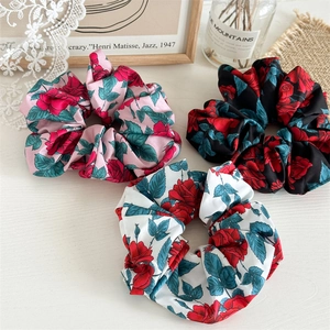Three silk rose print scrunchies in pink, black, and white on a decorative white surface