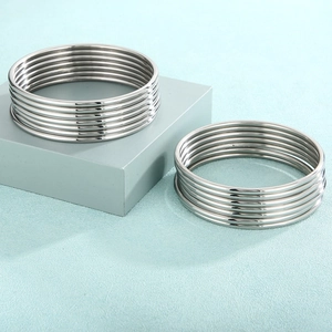 Detailed close-up of stacked minimalist silver stainless steel bangles on a blue surface