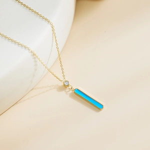 Detalle de collar de cadena dorada con colgante rectangular azul y circón pequeño