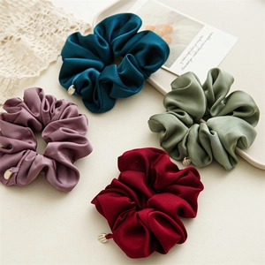 Detail of premium satin scrunchies in four elegant colors with metallic logo charm