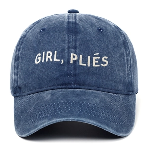 Détail de la broderie blanche GIRL PLIÉS sur une casquette en denim bleu délavé