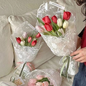 Close-up of elegant tulip bouquet wrapped in white lace fabric with decorative ribbons