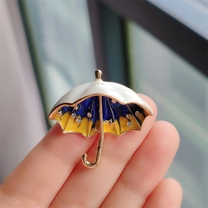 Detailed close-up of a golden umbrella brooch with blue enamel and sparkling rhinestones