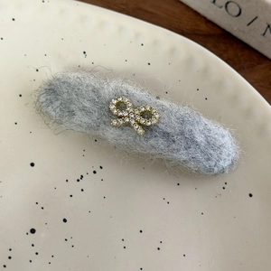 Detailed view of gray plush hair clip with a golden rhinestone bow on a ceramic plate