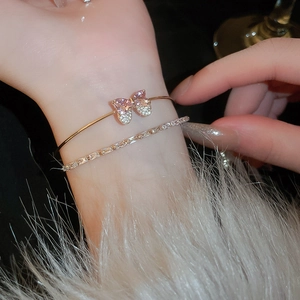 Detail of layered gold bracelet with pink crystal bow and sparkling zircon chain on wrist