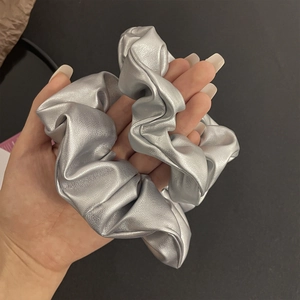 Macro view of a metallic silver y2k style PU leather scrunchie held in hand