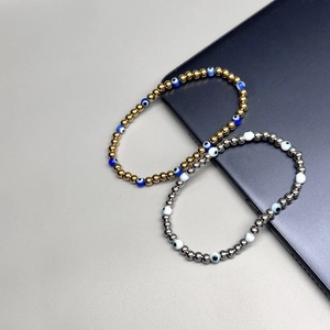 Detail of gold and silver beaded elastic bracelets with evil eye charms on a dark surface