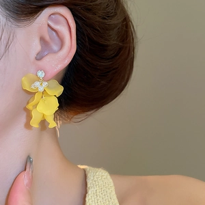Dettaglio di orecchini a fiore con petali gialli e perle bianche su una modella donna