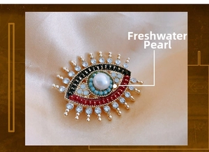 Close-up of eye-shaped brooch with freshwater pearl and crystals on silk background