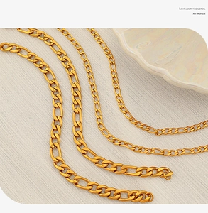 Detail of four golden Figaro chains in varying thicknesses on a beige fabric background