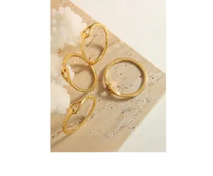 Detailed view of four minimalist gold-plated twisted rings on a beige travertine stone
