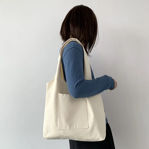 Detail view of a beige canvas tote bag with a large front pocket shown on a shoulder