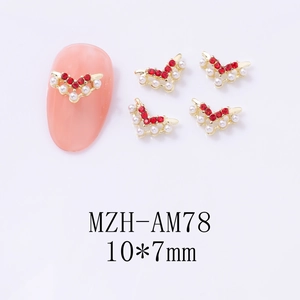 Detailed view of V-shaped gold nail charms with red rhinestones and white pearls, size 10x7mm
