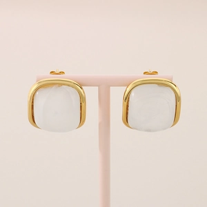 Détail de boucles d'oreilles carrées en résine marbrée avec cadre doré sur un support rose